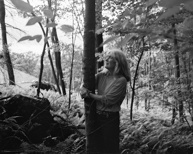 woman with her arms around a tree, standing in wooded area