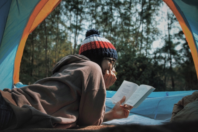 A camper reads in their open tent while facing out towards the woods