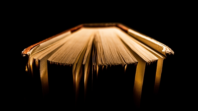 A photograph of a book in a dark room with light illuminating the tops of its pages