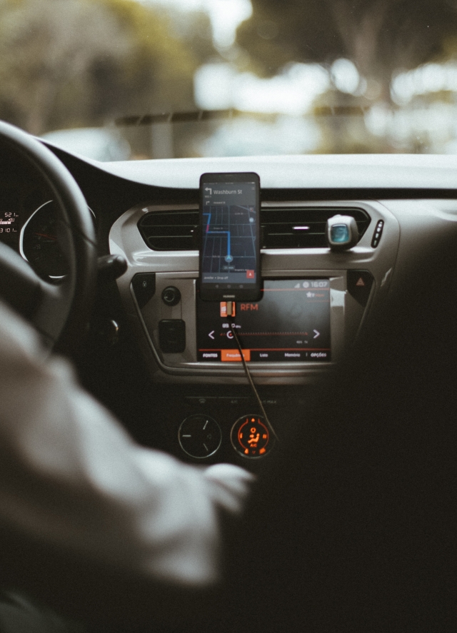 A car dashboard with a mounted smartphone with the Uber app on the screen, as seen from the backseat of the car