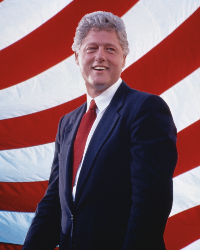 Bill Clinton standing in front of the red and white stripes of an American flag