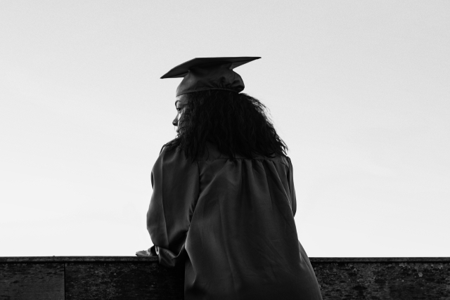 A woman dressed in a cap and gown gazes out into a empty background.