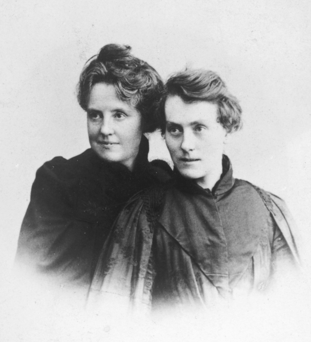 A photographic portrait showing Katharine Bradley and Edith Cooper with a white background and vignette border. Bradley and Cooper pose next to each other with their gazes turned in the same direction, slightly away from the the camera.