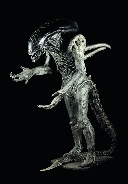 Alien costume standing with arms out on an empty black background