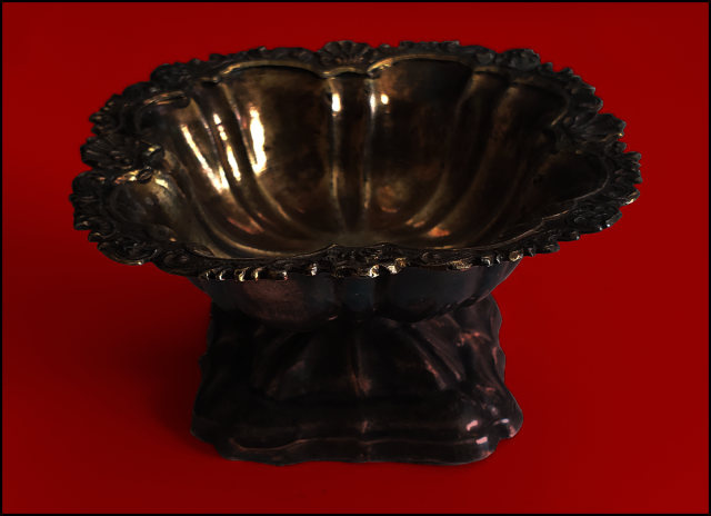 Dimly lit decorative metal urn on deep red background, low contrast, low accessibility.