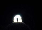 A person stands in silhouette at the bright entrance of a dark tunnel