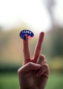 Photo illustration with a hand making a peace sign with a generic United States voting sticker stuck to the index finger. The sticker reads “I lost” instead of “I voted”. 